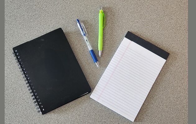 Notebook, pens, and notepad on a desk surface.