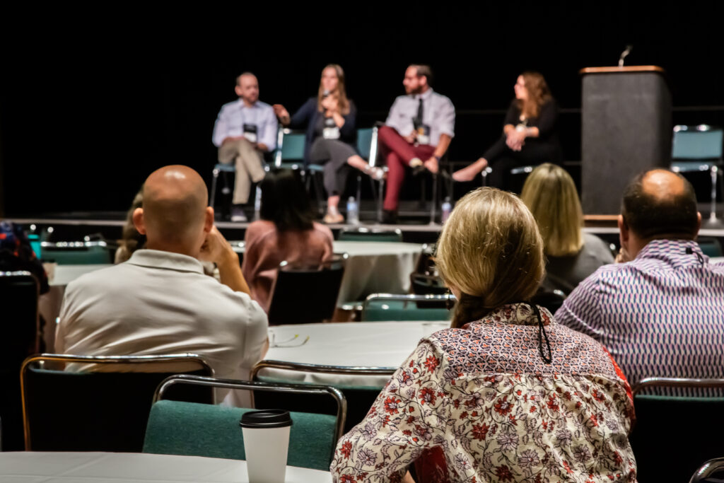 Panel discussion with four speakers on stage and an attentive audience.