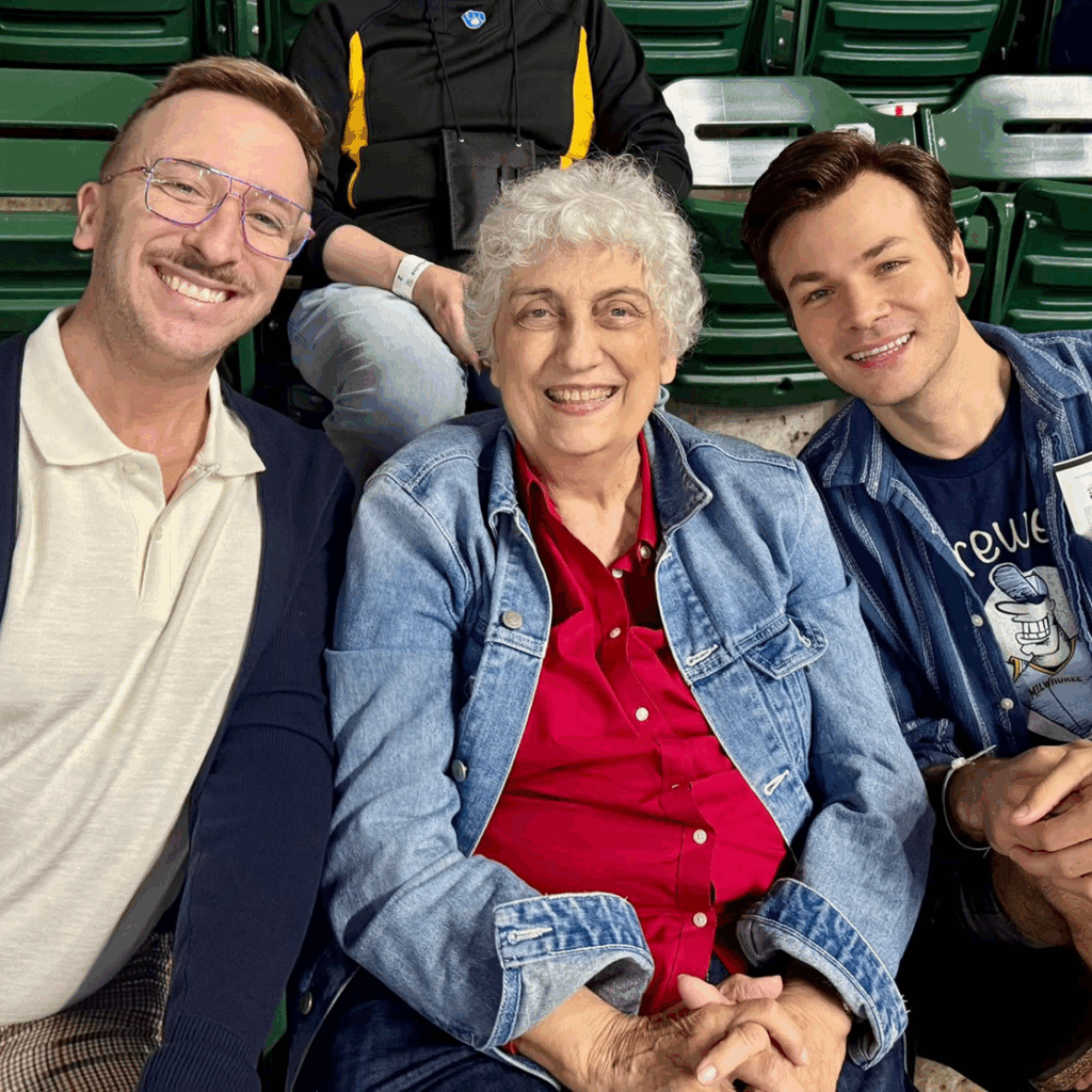 Three people smiling and sitting closely together on stadium seats.